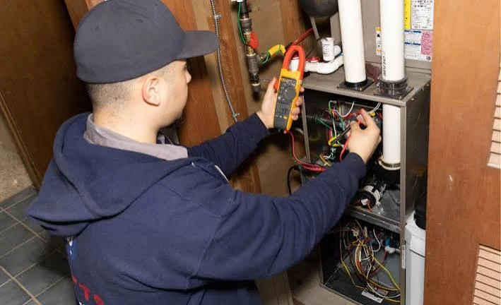 Technician using a clamp meter to test heating-system wiring and controls