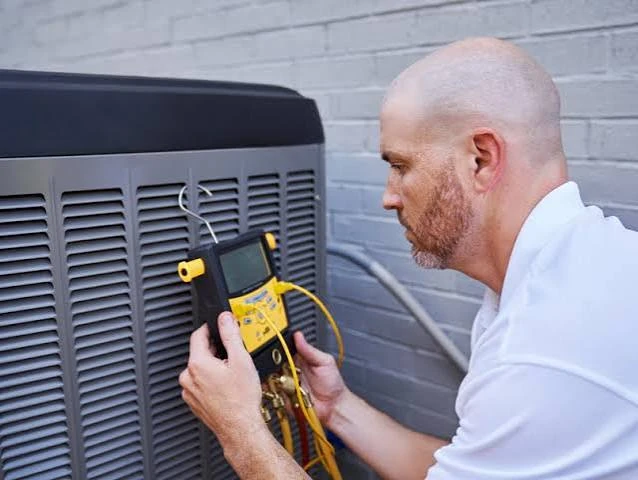 Technician using a digital multimeter to diagnose outdoor air conditioning equipment