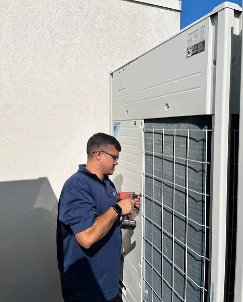 HVAC technician servicing a tall outdoor heat-pump unit